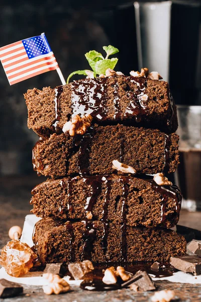 Homemade dark chocolate brownies topping with nut slices and mint stacked on dark table