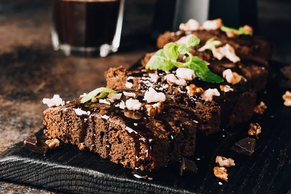 Homemade dark chocolate brownies topping with nut slices and mint stacked on dark table