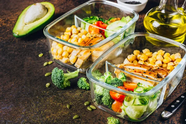 Healthy meal prep containers with chickpeas, chicken, tomatoes, cucumbers, avocados and broccoli. Top view