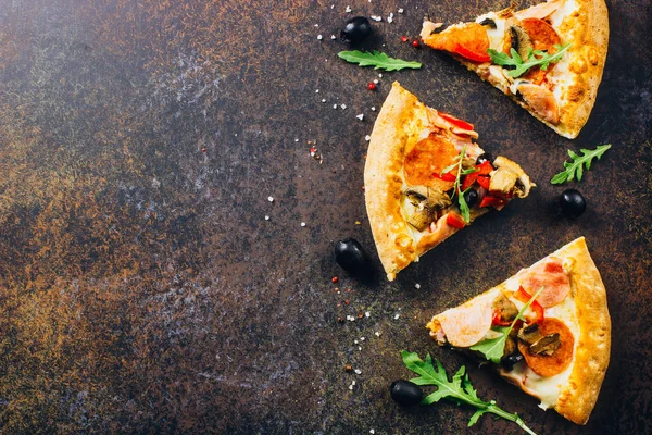 Slices of pizza with prosciutto and rocket salad with spices on black background. Pizza is cooking in the oven. Pizza menu. View from above. Space for text.