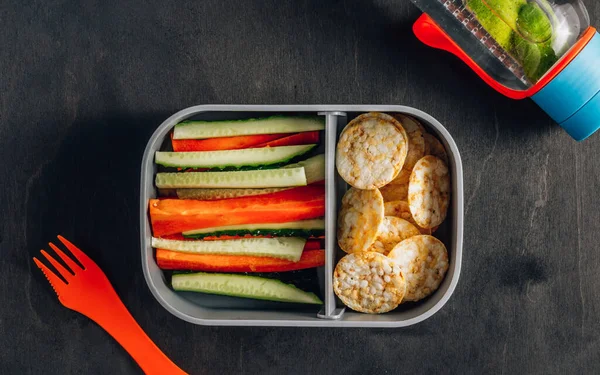 Home prepared meal container. Snack Box with cucumber and carrot sticks, healthy rice and corn crackers for work place or schools. Gluten-free diet.