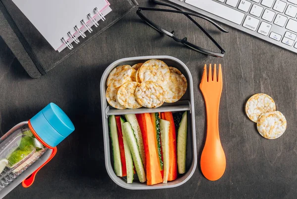 Home prepared meal container. Snack Box with cucumber and carrot sticks, healthy rice and corn crackers for work place or schools. Gluten-free diet.