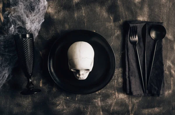 Festive Halloween table setting in a black style. Plate with fork, spoon and knife on a linen napkin and Skull candle holder. Halloween dinner. Minimal concept. Top view. Flat lay — Stock Image Festive Halloween Table Setting Black Style Plate Fork Spoon Knife Royalty Free Stock Photos