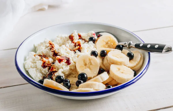 Organic cottage cheese with date syrup and banana for healthy breakfast. White wooden table. Selective focus