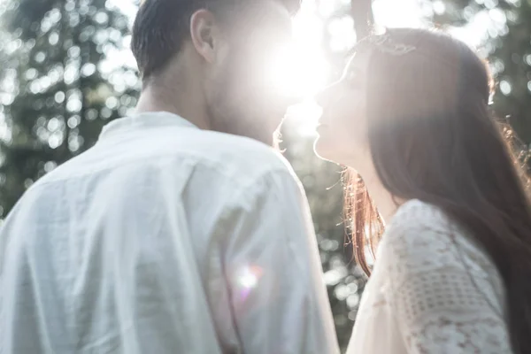 Young beautiful Slavic couple in love walks through the woods, sweet girl in a simple boho-style wedding dress. They are happy and calm. Golden hour, summer day, warm. They kiss, hug and hold hands.