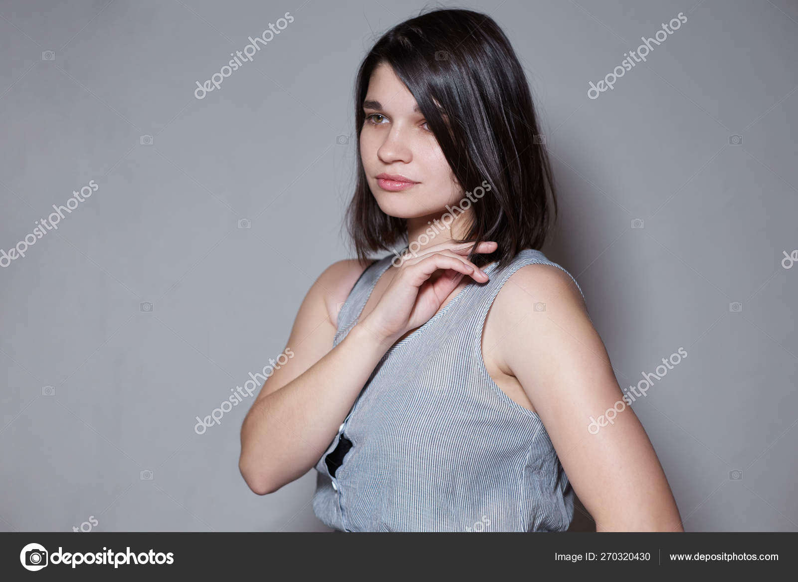 A pretty brunette with hair just below the shoulder, straightens her hair,  she is beautiful and very feminine, looking at the camera, close-up. Stock  Photo by © 270320430