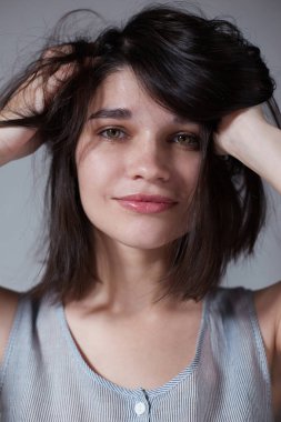 Omzunun hemen altında saçları ile güzel bir esmer, saçlarını düzleştiren, o güzel ve çok kadınsı, kamera bakarak, yakın çekim.