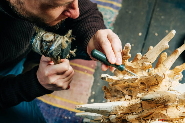 A man master woodcarver creates a sculpture of wood with a chisel and hammer