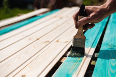 Kaplama astar panoları ahşap yüzeyine renkli koruyucu boya ile. El bir fırça ile güneşli havalarda açık havada bir parlak turkuaz yüzey boyar.