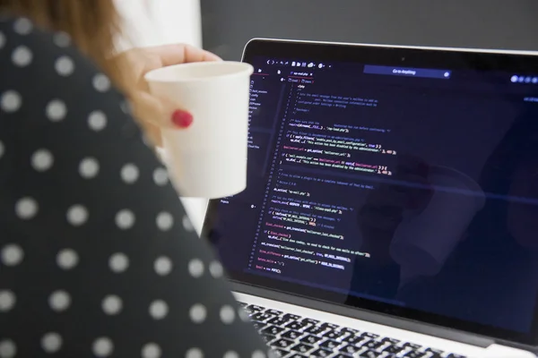 Programadora mujer con taza de café trabajando en computadora portátil en la oficina — Foto de Stock