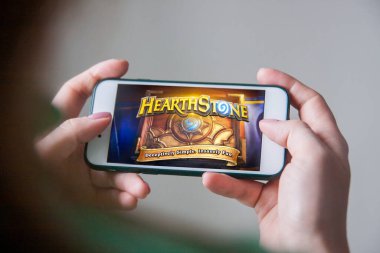 Los Angeles, Kaliforniya, ABD - 25 Şubat 2019: Hearthstone giriş ekranında akıllı telefonu tutan eller