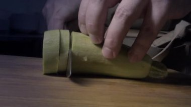 Ahşap mutfak tahtasındaki bir şef tarafından bıçakla kabak dilimlemek, aşçının elleri.