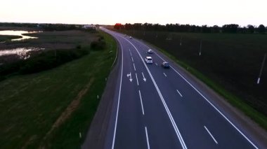 Karayolu trafik arabalar karayolu üzerinde. Yeşil buğday alanları bir yükseklikten Rusya Federasyonu Krasnodar asfalt yol gün batımında. Quadrocopter ile çekim.