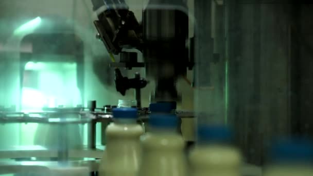 Η αυτόματη συσκευή περιστροφές το πώμα της φιάλης. Αυτοματοποιημένη γραμμή για την παραγωγή του γάλακτος σε πλαστικά μπουκάλια. Μπουκάλια γάλα σχετικά με μια μεταφορική ταινία. — Αρχείο Βίντεο