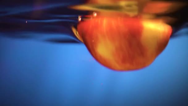 La mela cade in acqua. Mela rossa cade in acqua, primo piano, sfondo grigio, super slow motion — Video Stock