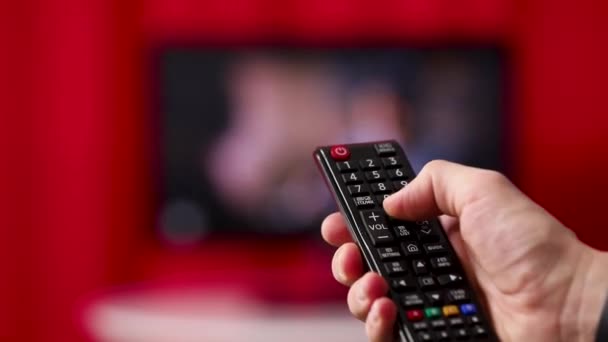 Ruce držte dálkového ovládání televizoru. TV na pozadí. — Stock video