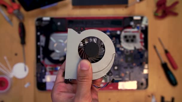 Repairman holding a cooler cooling on the background of a dismantled laptop. — Stock Video