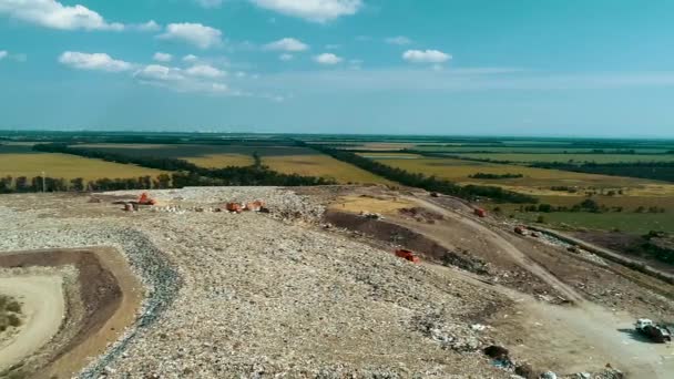 Discarica sullo sfondo di campi verdi. Attrezzature per lo smaltimento dei rifiuti vanno sulla discarica stradale. Un gabbiano che gira intorno. Una vista enorme spazzatura discarica dal drone . — Video Stock