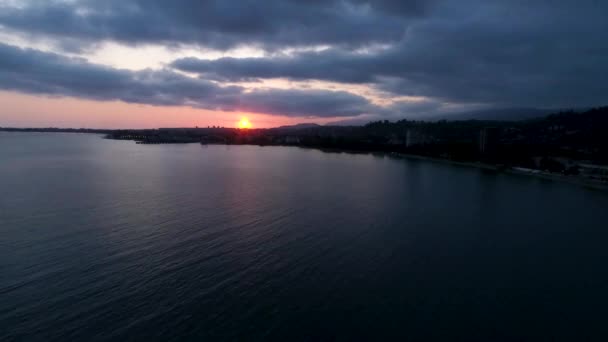 夕暮れ時の太陽地平線上の海の海岸の都市景観の夕日に反映されます。スフミ(アブハジア). — ストック動画