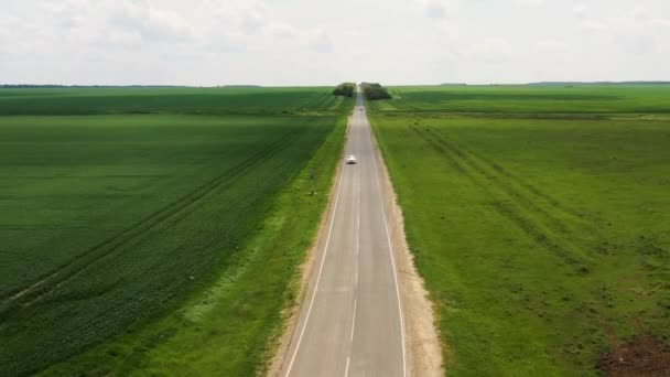 El movimiento de un coche blanco en la carretera entre los campos. Disparo horizontal desde el dron . — Vídeos de Stock