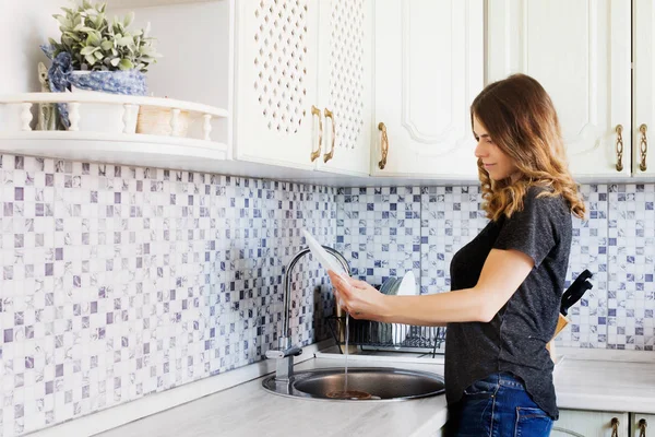 Pretty young woman washing dishes. Housewife in the kitchen.