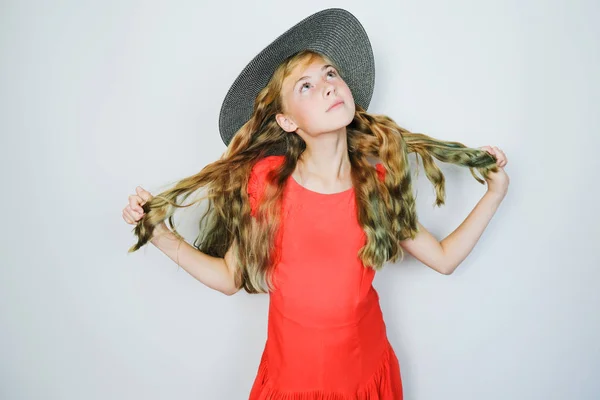 Attractive caucasian teen girl in red dress and hat looking up dreamily.
