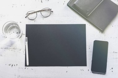 Mockup boş siyah kağıt levha, smartphone, gözüne gözlük, doğal beyaz otantik ahşap masa üzerinde. İş boş mock-up arka plan mesaj yazmak için. Üstten görünüm, bokeh.