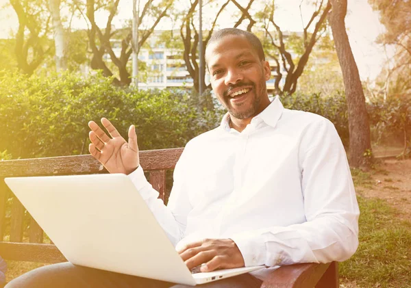 Jovem empresário africano americano em roupas informais trabalhando na rua ensolarada em laptop, verificando e-mail. Fundo desfocado . — Fotografia de Stock