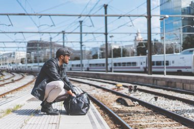 Tren istasyonunda bir platform yanında yürüyen bir sırt çantası önünde bir giysi çanta ile sahip çekici emin İspanyol adam.