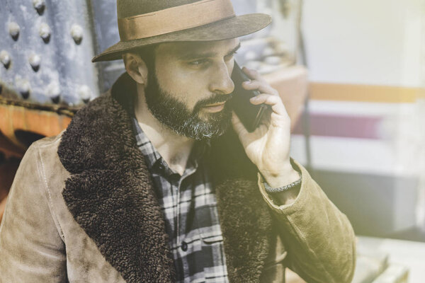 Bearded Man in hat talking on a mobile phone.Outdoor portrait of modern guy with mobile smartphone outside at the railway platform waiting for the train.