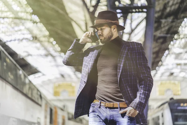 Joven empresario hispano confiado sosteniendo el teléfono inteligente en su mano y llamando mientras está parado en la plataforma ferroviaria esperando el tren — Foto de Stock