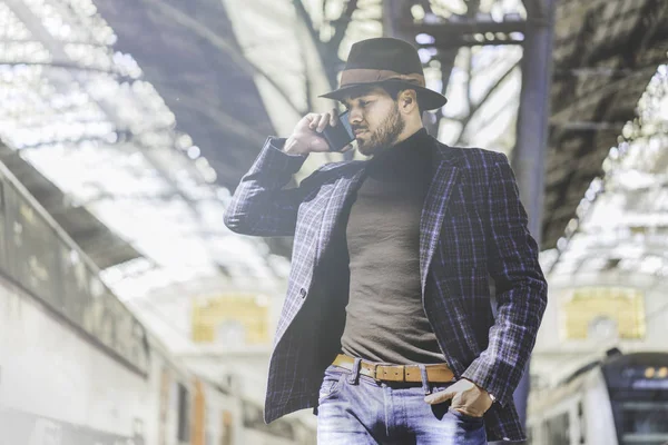 Atractivo joven empresario hispano confiado sosteniendo un teléfono inteligente en su mano y llamando mientras estaba parado en la plataforma ferroviaria esperando el tren — Foto de Stock