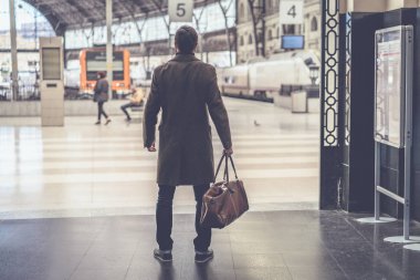 Seyahat çantası Tren İstasyonu salon ile ayakta ve onun tren seyir emin yetişkin adam.