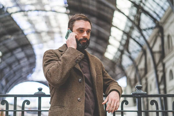 Empresario barbudo haciendo una llamada en su teléfono móvil.Empresario profesional casual usando teléfono inteligente en la sala de la estación de tren . — Foto de Stock