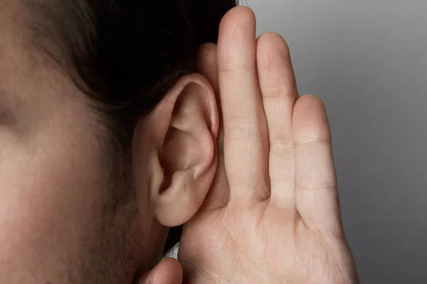 Le mâle qui écoute tient sa main près de son oreille sur un fond gris. . — Photo