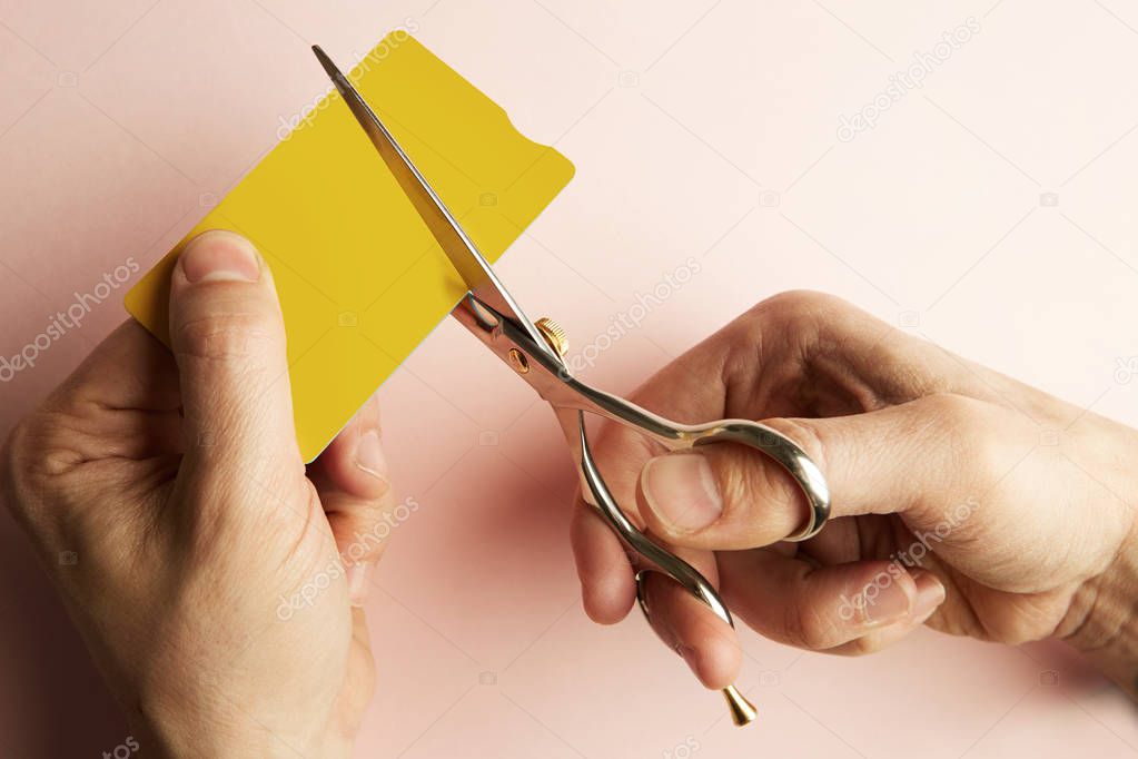 Mockup of yellow color credit card cutting male hands with scissors on empty pink desk. Business mock-up background for message writing.Top view. Horizontal.