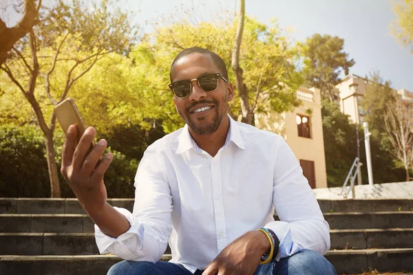 Young attractive african man holding hand on smartphone while sitting at sunny city park.Concept of happy business people working outside Stock Picture