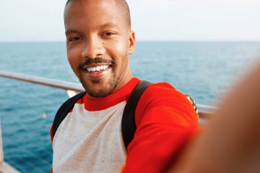 Genç Afro-Amerikan hipster adam alarak selfie mutlu yüzü açık havada şehir ile gülümseyen yakışıklı. Mavi arka plan bulanık denizde.