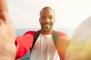Mutlu yüz açık havada City ile iki el selfie alarak gülümseyen genç Afro-Amerikan hipster yakışıklı. Mavi deniz üzerinde arka plan bulanık. Mercek parlamaları.