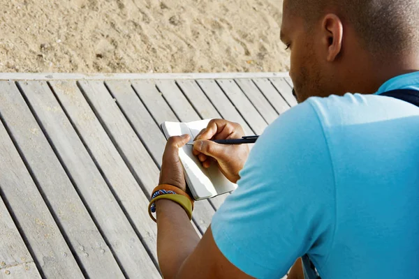 Atractivo vestido casualmente joven hombre africano americano haciendo notas en copybook. Estudiante preparándose para la lección en la universidad . —  Fotos de Stock