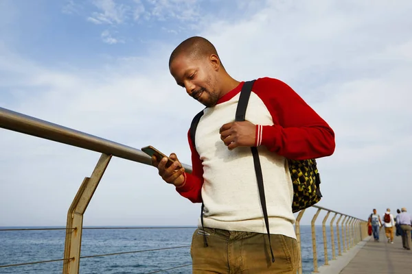 Atractivo joven viajero afroamericano que utiliza la mano del teléfono móvil al aire libre de la ciudad. Cielo nublado sobre fondo borroso . —  Fotos de Stock