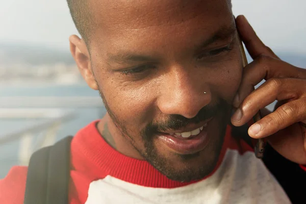 Hombre afroamericano usando teléfono móvil en la playa. Joven feliz sonriente hombre hipster urbano con ropa informal y el uso de teléfono inteligente . —  Fotos de Stock