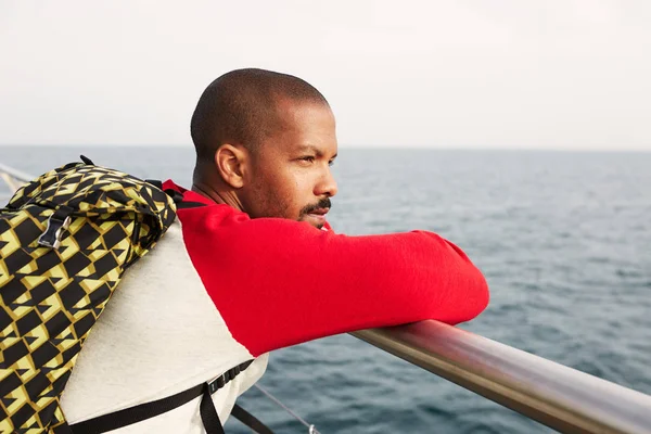 Atractivo joven afroamericano hipster hombre con mochila soñando en la playa y disfrutando de la vista al mar.Primer plano retrato —  Fotos de Stock