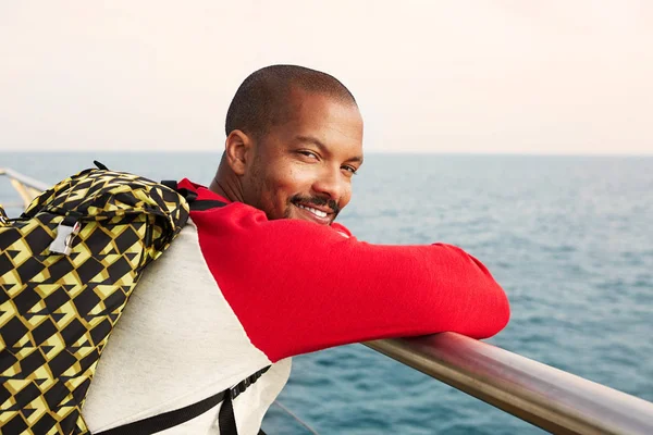 Feliz joven afroamericano hipster hombre con mochila soñando en la playa y disfrutando de la vista al mar.Primer plano retrato —  Fotos de Stock