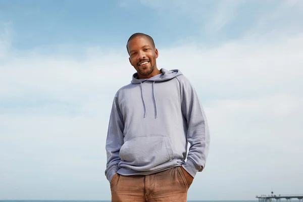 Summer active sports concept. Smiling happy young African-American man hipster in sport hoody on the beach. Stock Image