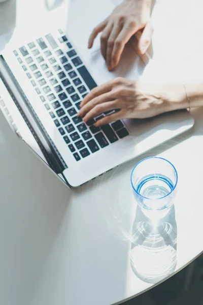 Werkende momenten thuis. Jonge vrouw te typen op laptopcomputer zittend aan de houten tafel in licht gekleurd woonkamer van moderne huis. Verticaal. — Stockfoto