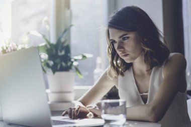 Modern evin oturma odasında masada oturan bir dizüstü bilgisayar üzerinde çalışan mutlu rahat güzel kadın. Film etkisi.