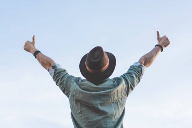 Yakışıklı mutlu mavi gökyüzüne bakarak hipster sakallı ve onun ellerinde ok sembolü jest. İnsanlar gözlem kavramı.