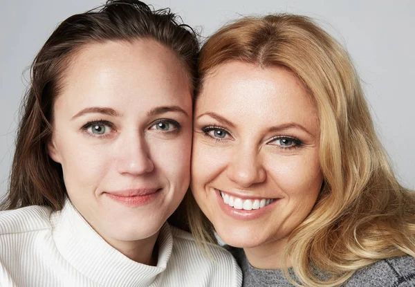 Two Young beautiful womens with blonde and brunette hair smiling on gray studio background.Medical and cosmetic facial skin healthcare concept. — Stock Photo, Image