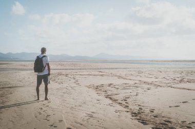 Aktif spor kas gündoğumu sırt çantası ile deniz kıyısında ayakta ve ufuk arayan adam sakallı.